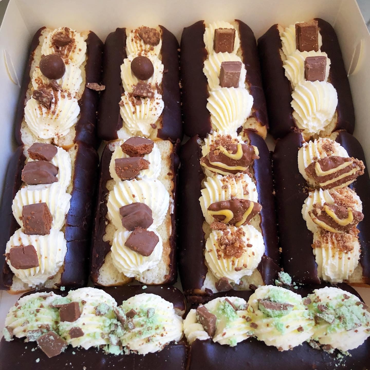 Chocolate-dipped eclairs topped with swirls of whipped cream and various chocolate candy bar pieces.