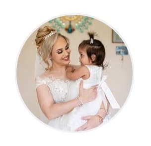 Smiling bride in a lace gown holding a young girl in a white dress.
