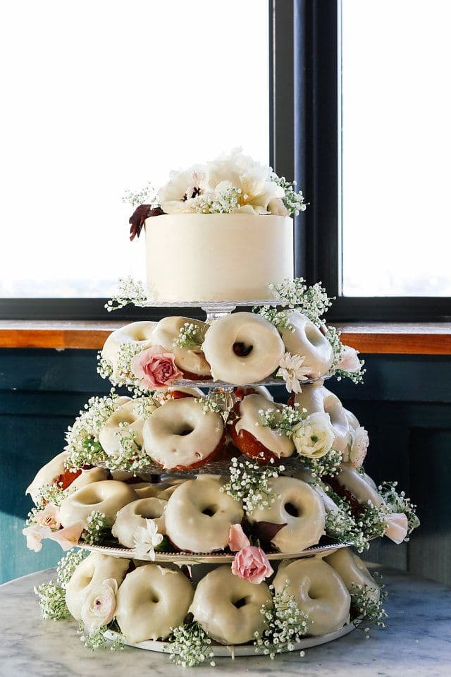 Tiered dessert stand with a white cake and glazed donuts decorated with fresh flowers.