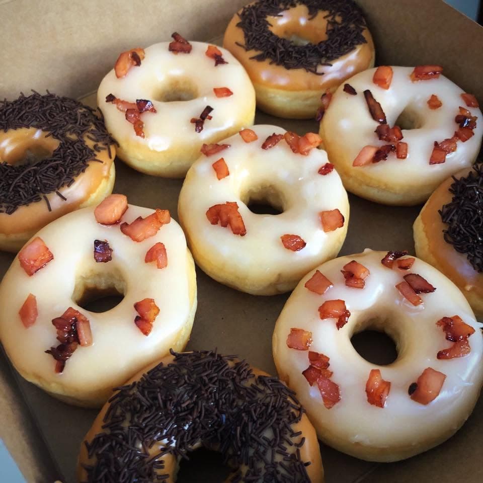 Box of donuts with white glaze and bacon bits and caramel glaze with chocolate sprinkles.