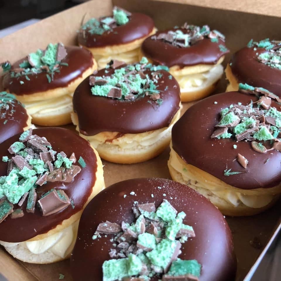 Box of cream-filled donuts topped with chocolate icing and crushed mint chocolate candy pieces.