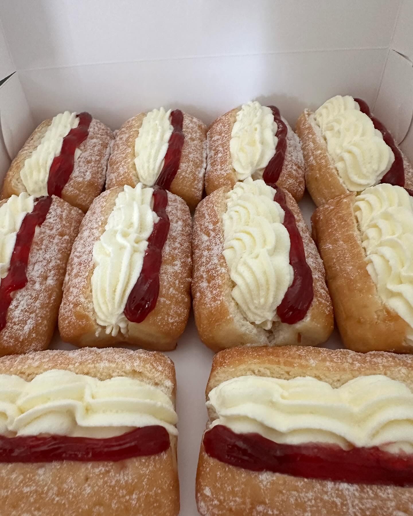 Rectangular cream buns with red jam and whipped cream, dusted with powdered sugar.